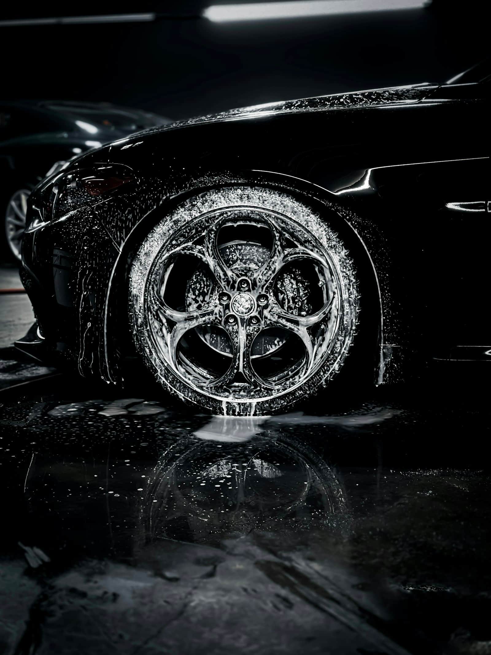 Foam rinsing down over a black car's wheel and fender in a dark wash bay
