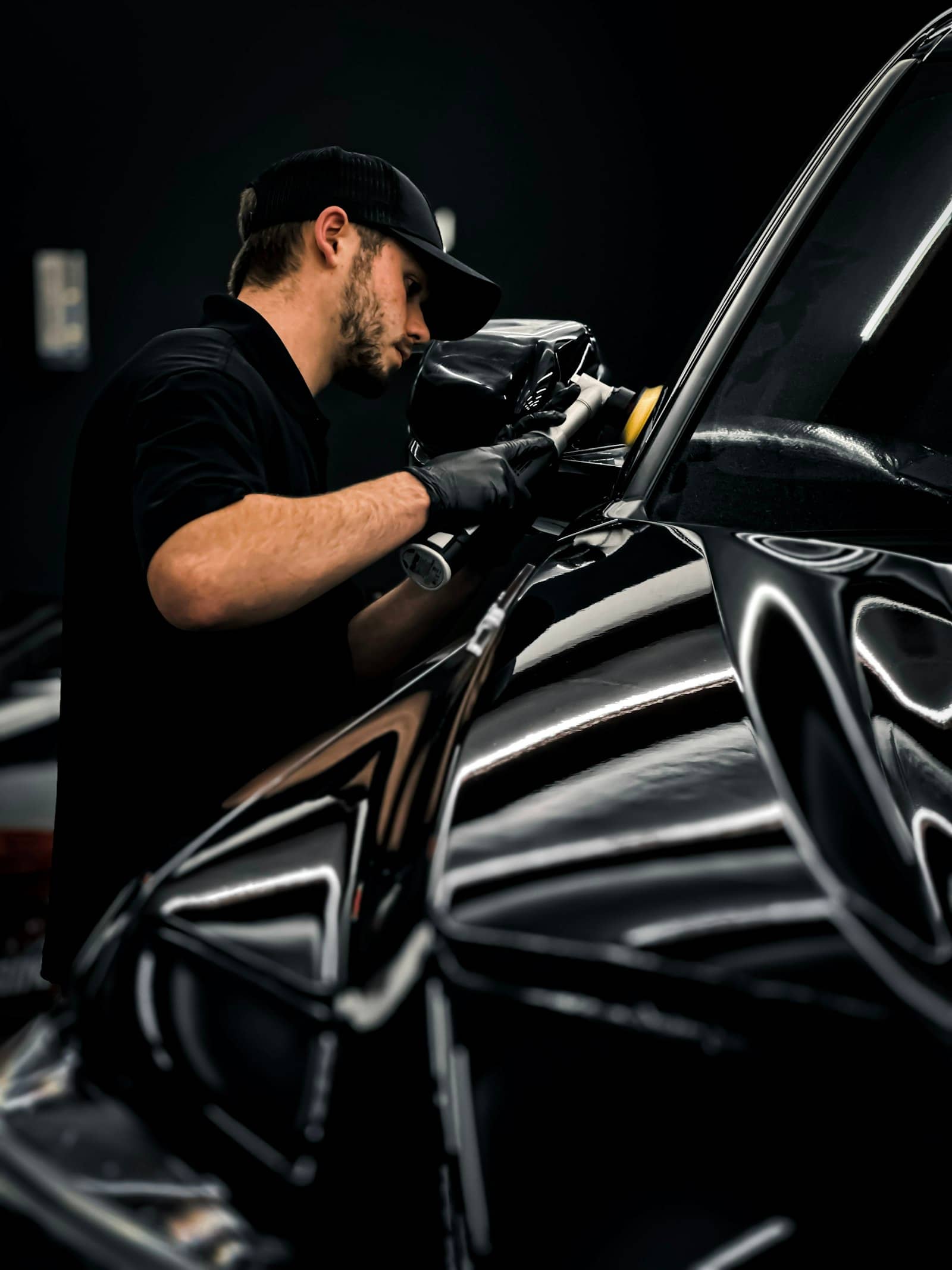 Detailer machine-polishing the hood of a black car in a dark studio