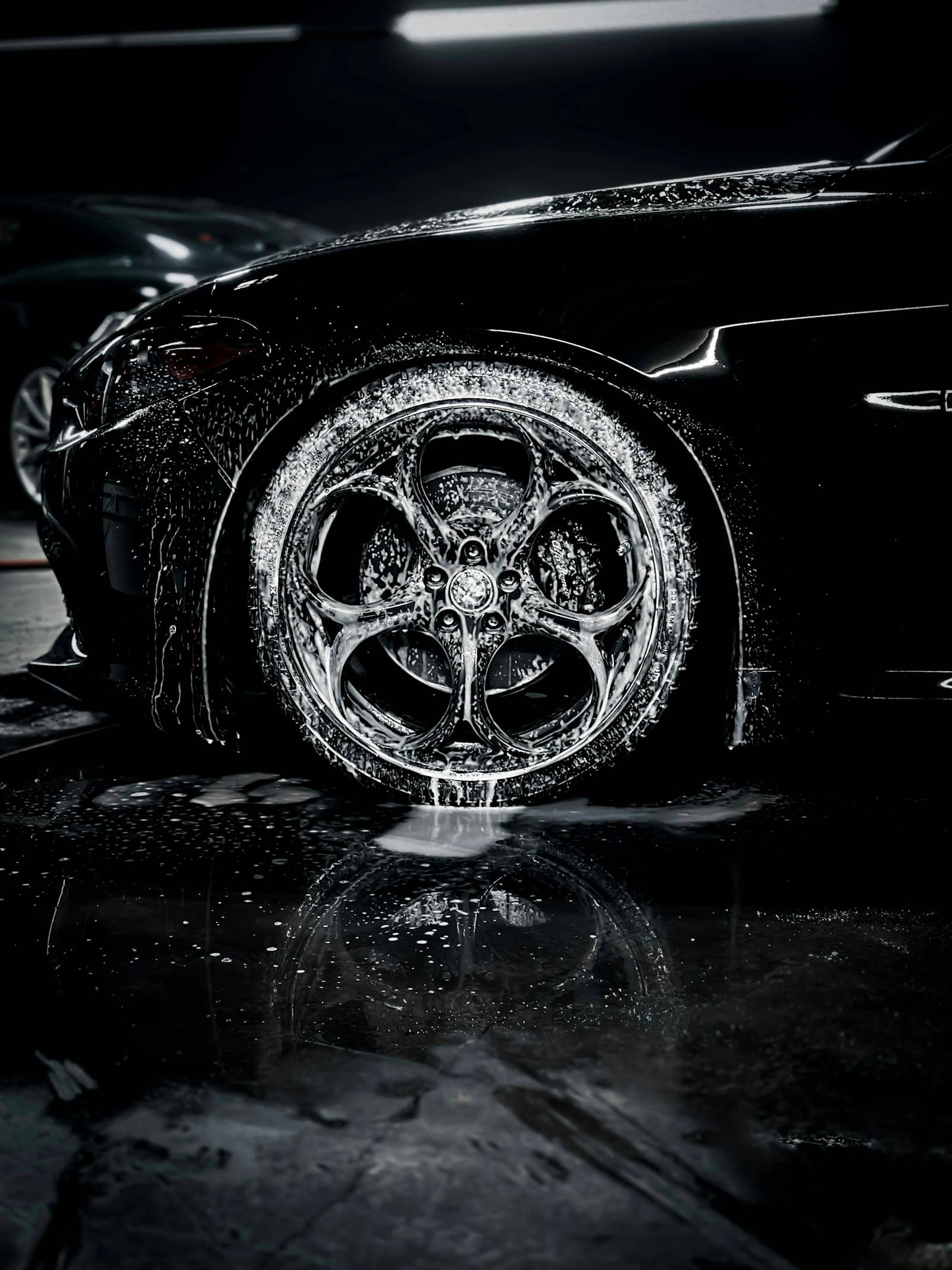 Foam rinsing down over a black car's wheel and fender in a dark wash bay