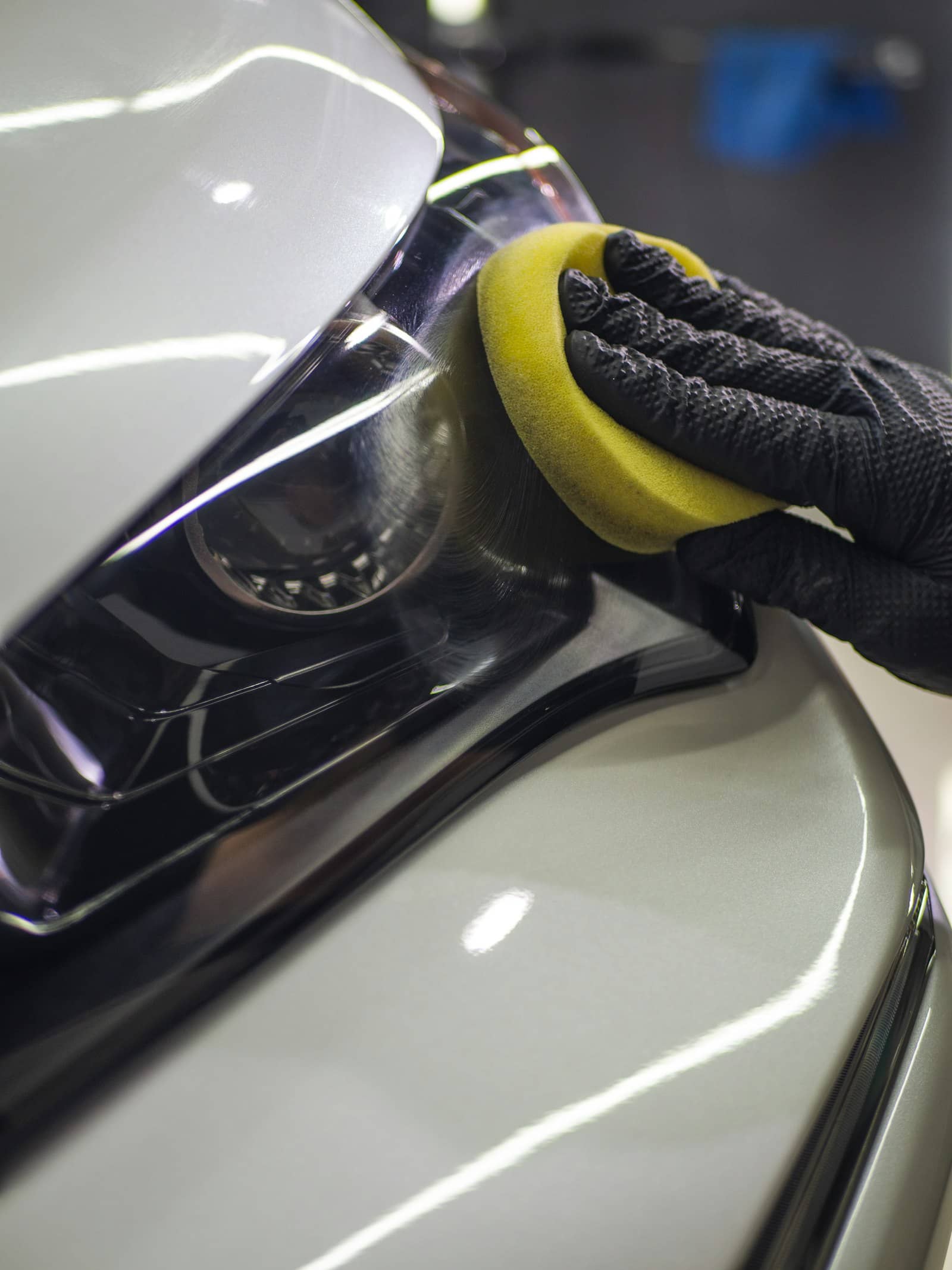 Gloved hand working a coating applicator pad across a headlight and front panel